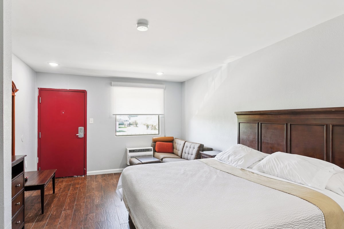A bedroom with a large bed, a red door, a window with a view, and a wooden headboard.