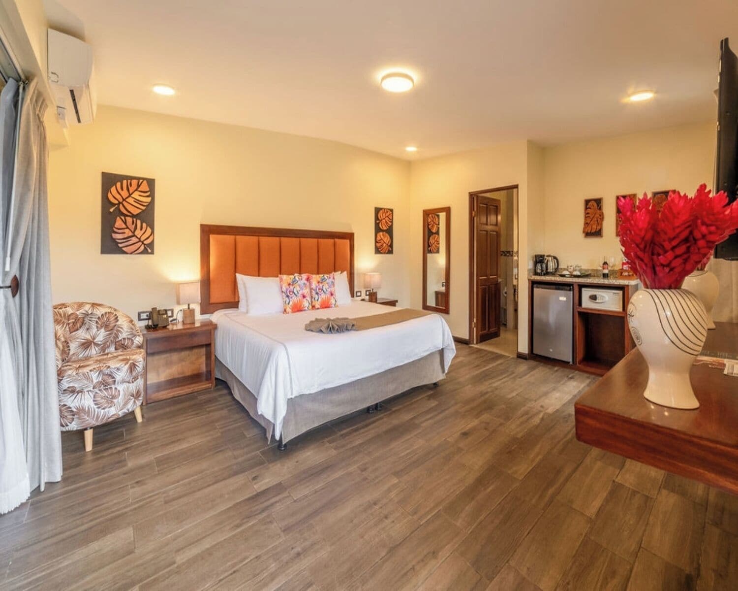 A hotel room with a bed, a desk, a chair, a small kitchenette, and a bathroom.
