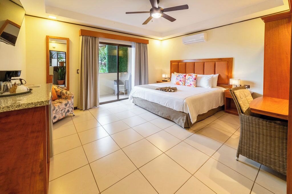 A hotel room with a bed, a desk, a chair, and a balcony with curtains.