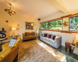 Una sala de estar moderna con un sofá, un sillón y un tapete grande. Se ve una ventana con vistas a follaje y un adorno en la pared.