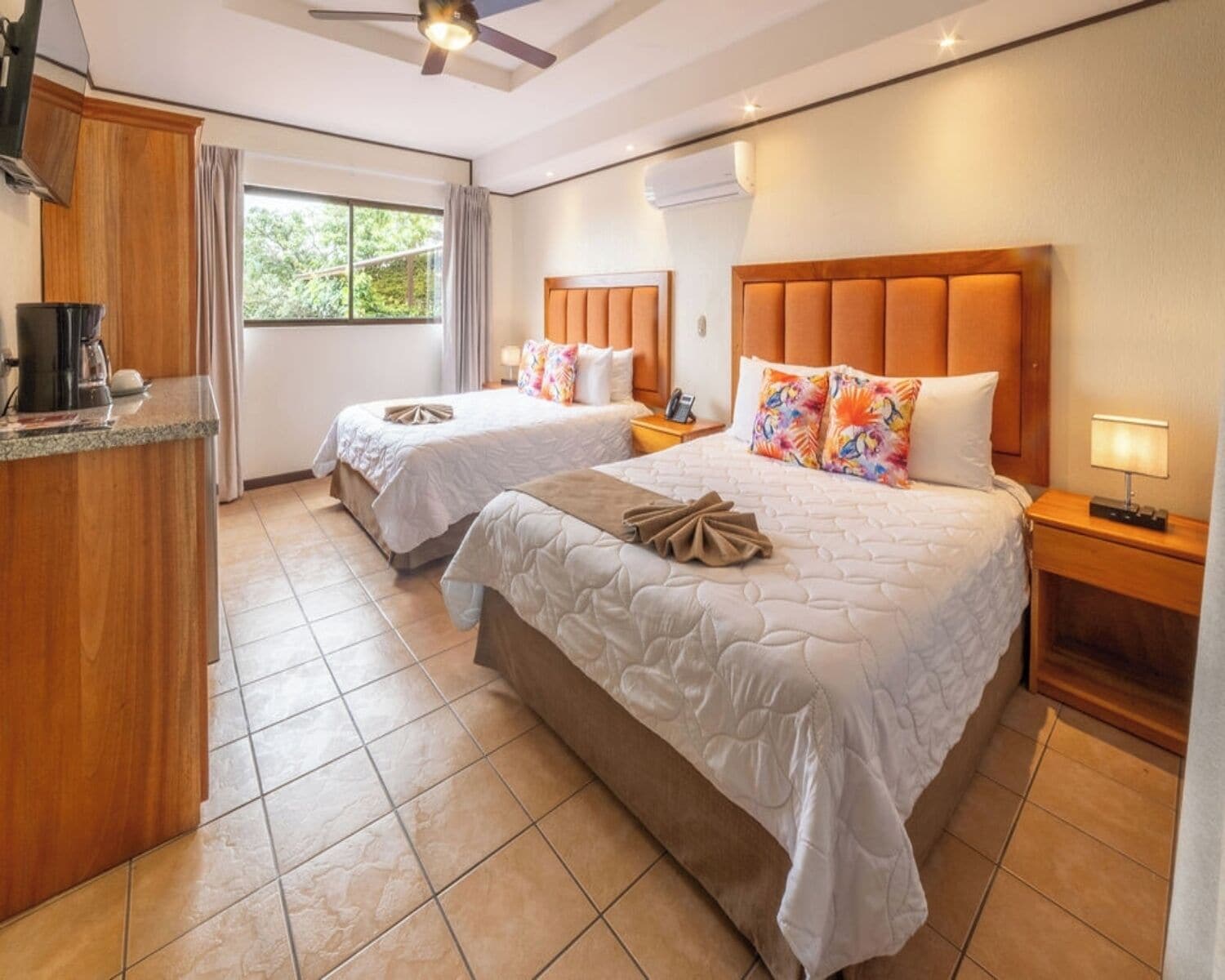 A hotel room with two beds, a kitchenette, and a window with curtains.