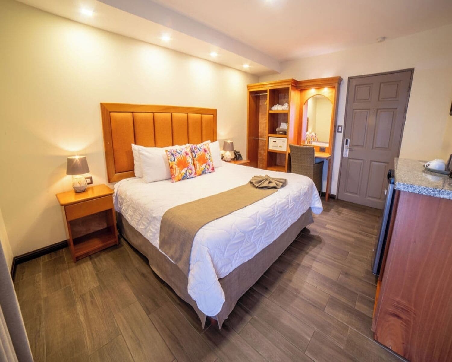 A hotel room with a large bed, a desk, a chair, a wardrobe, and a bathroom.