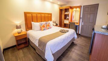 A hotel room with a large bed, a desk, a chair, a wardrobe, and a bathroom.