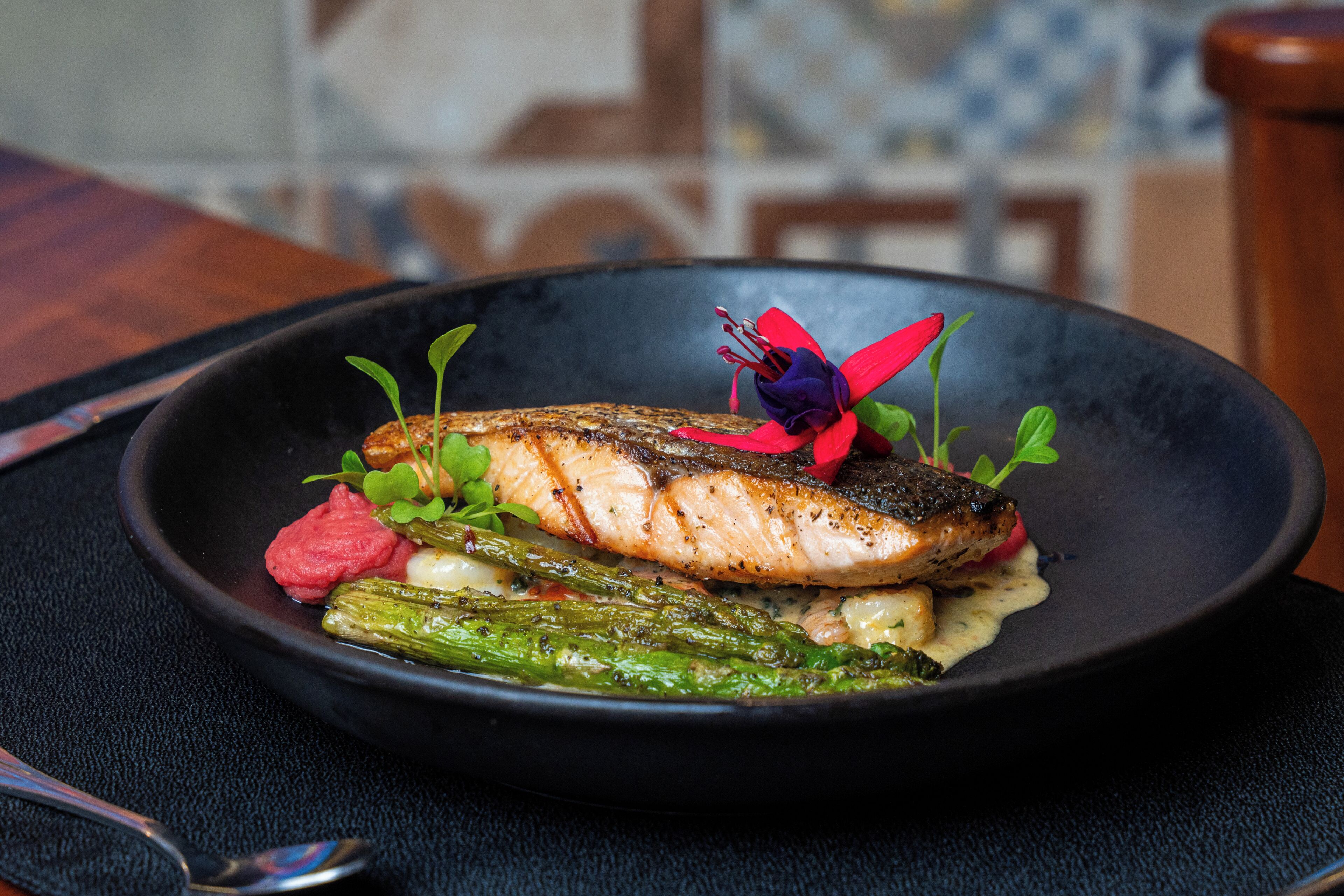 Un plato de comida con pescado, verduras y una flor decorativa.