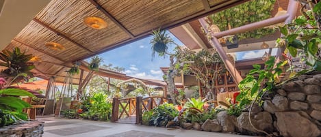 A covered outdoor area with a stone floor, bamboo ceiling, and various plants.