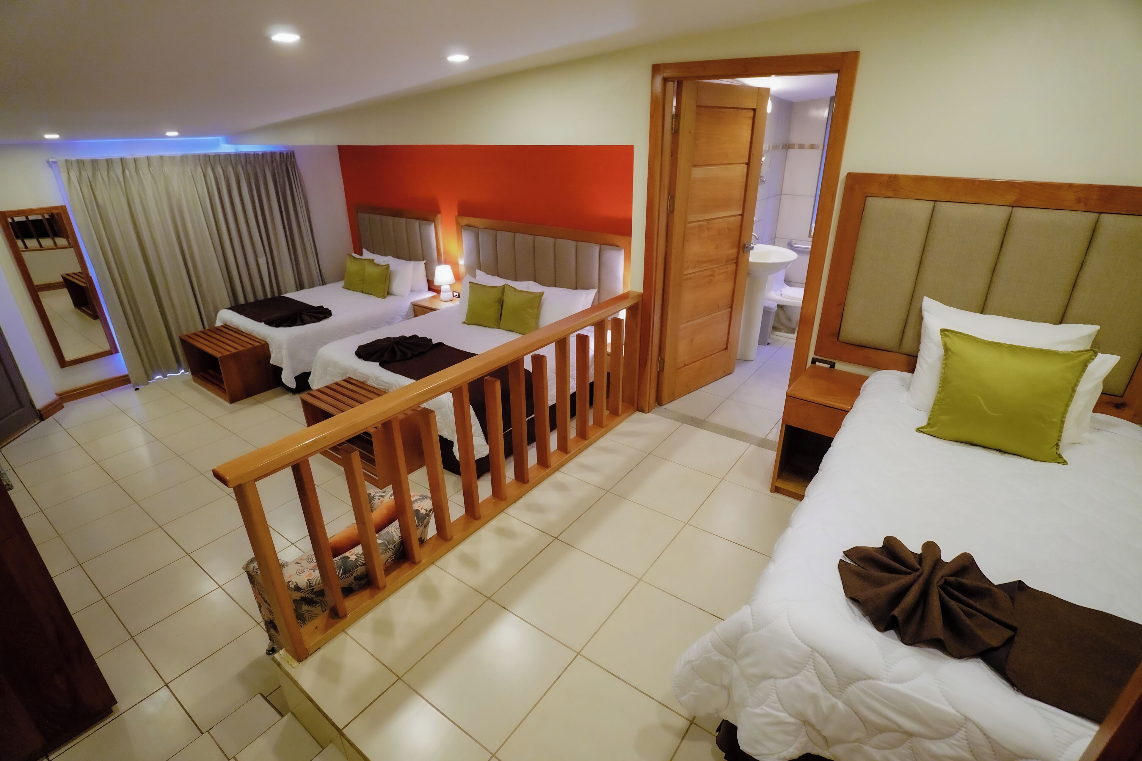 A hotel room with two beds, a wooden railing, a bathroom with a sink, and a mirror.