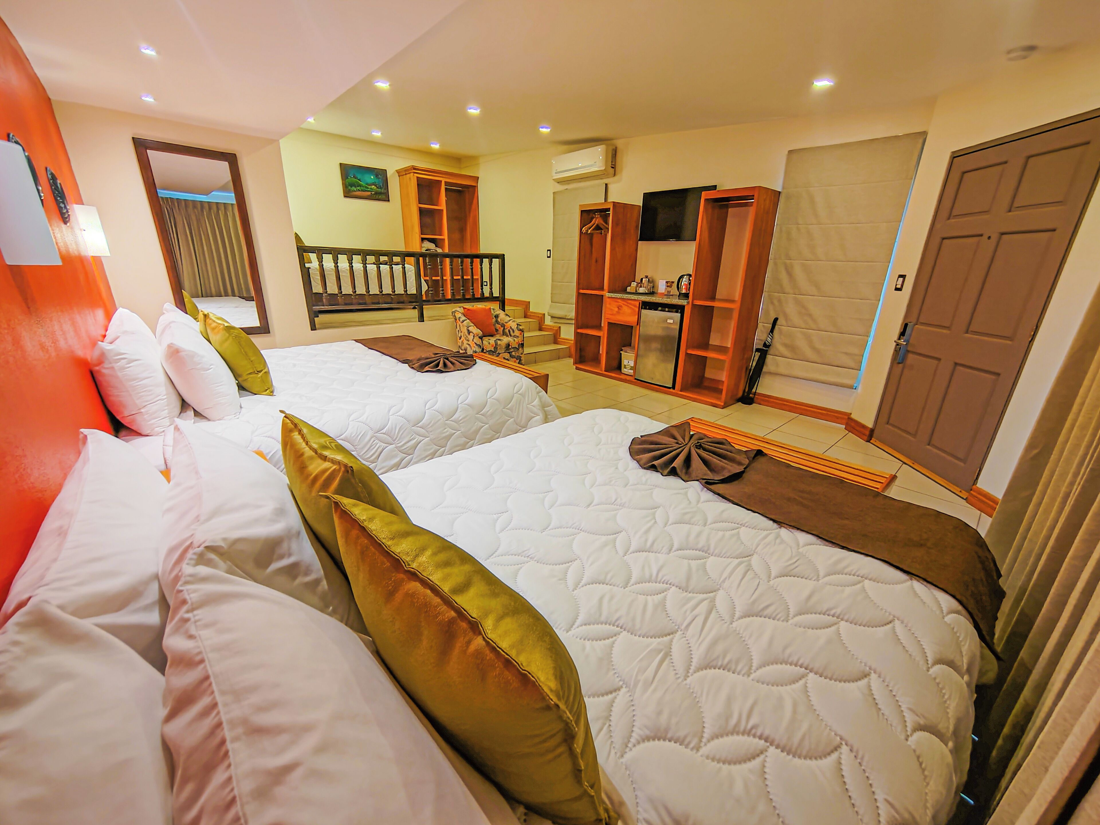 A hotel room with two beds, a staircase, a small kitchen area, and a door.