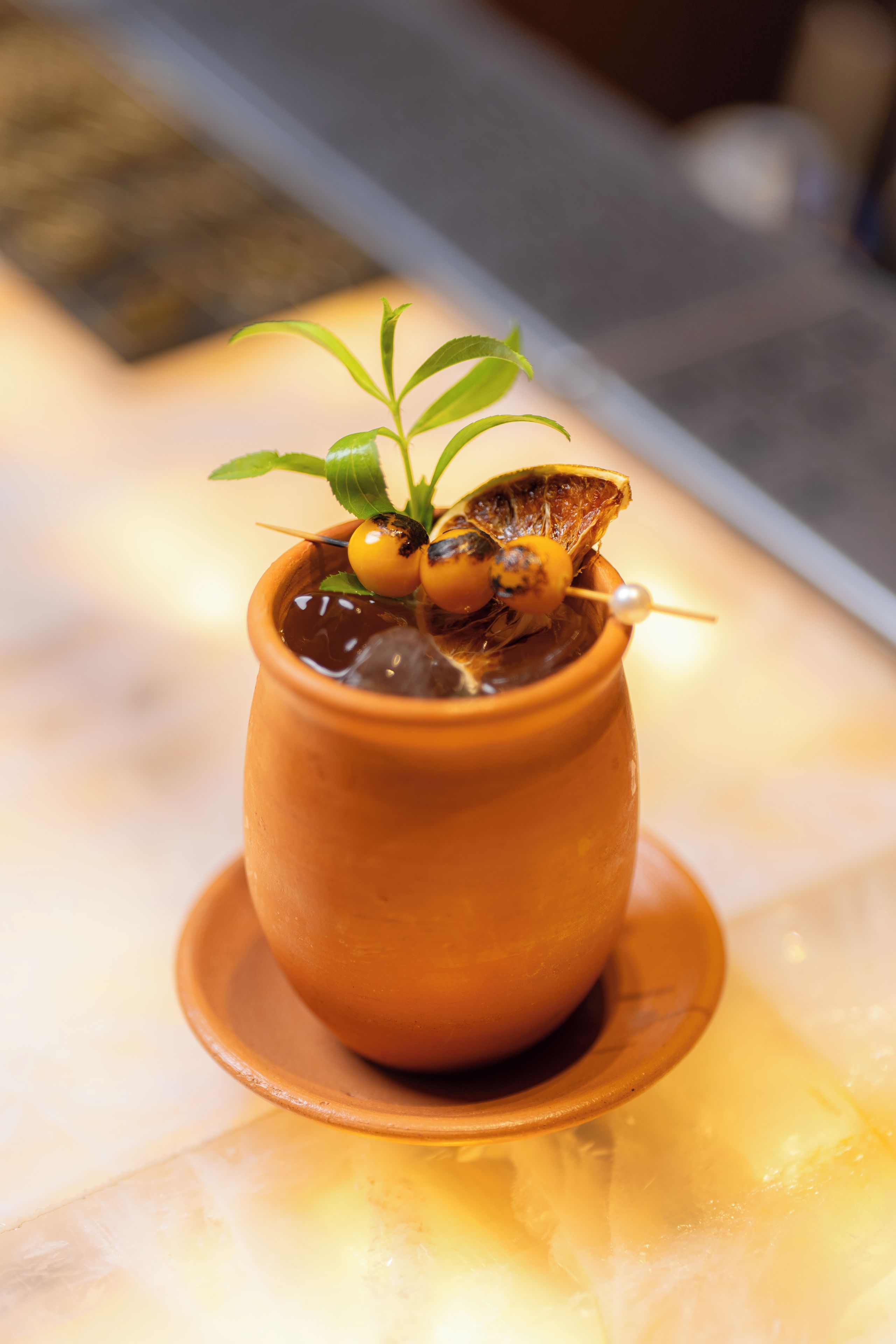 A terracotta pot with a plant and two yellow fruits on a saucer.