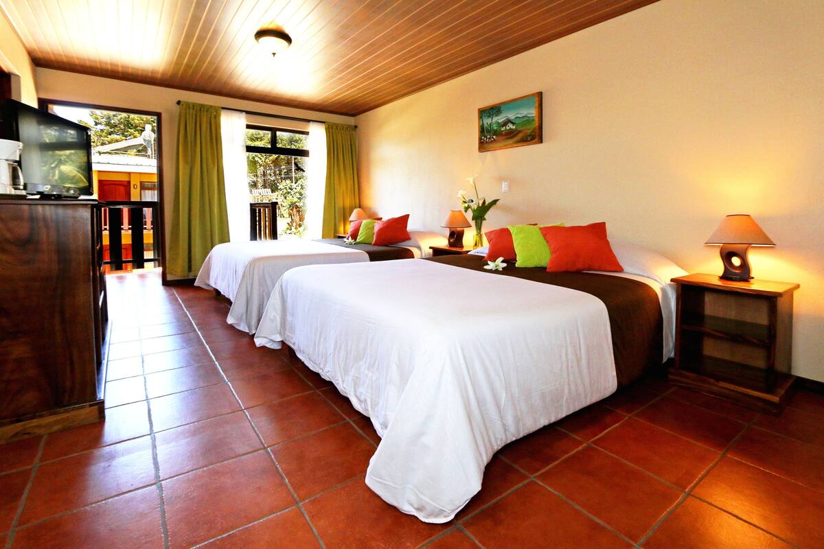 A hotel room with two beds, a TV, a desk, and a window with curtains.