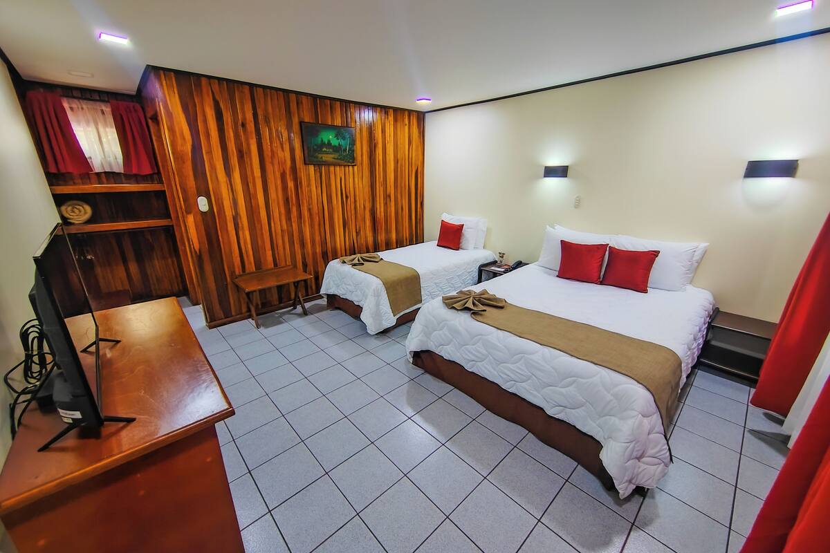 A hotel room with two beds, a wooden panel wall, a desk with a computer, and a TV.