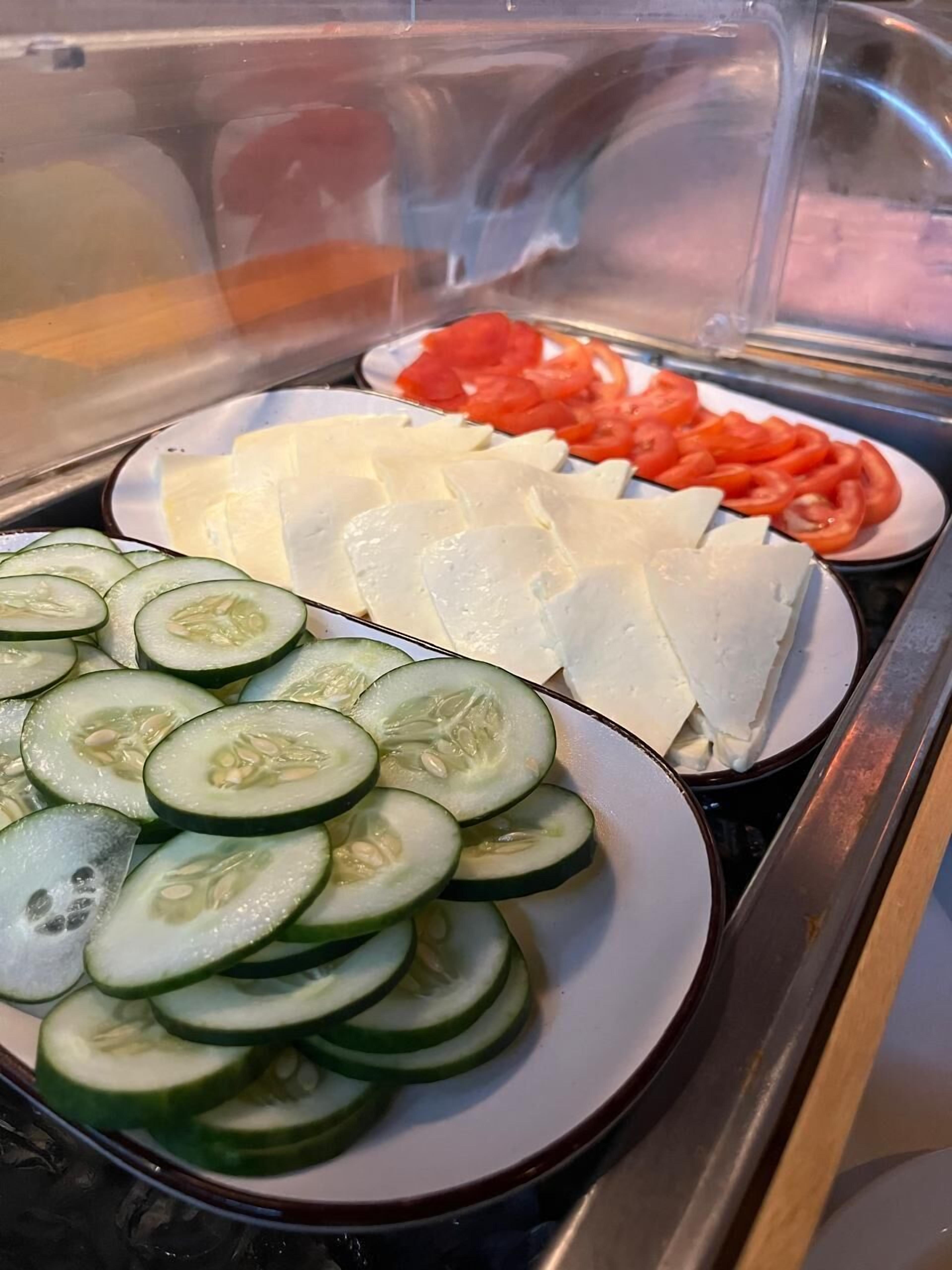 A buffet with sliced cucumbers, tomatoes, and cheese.
