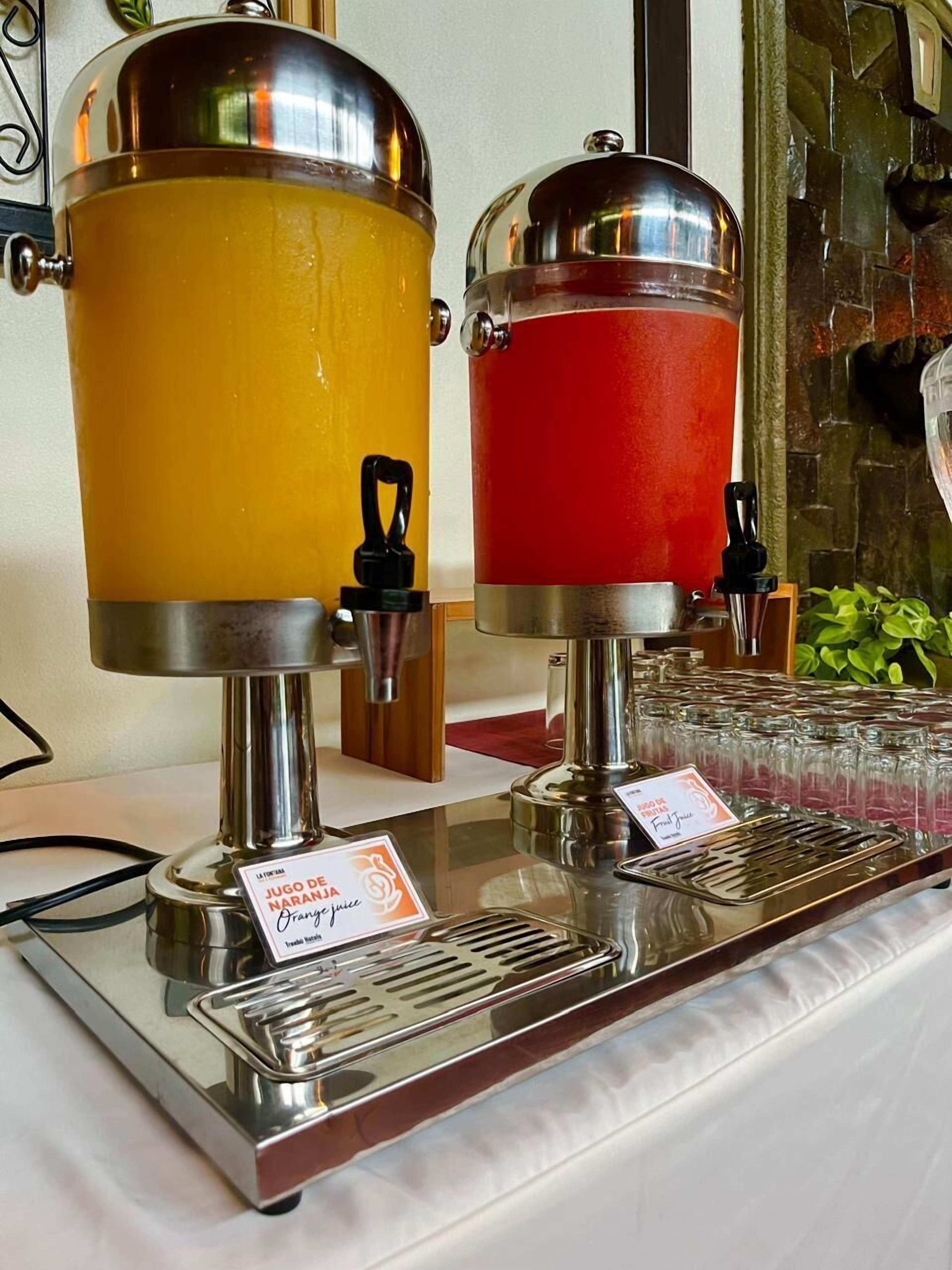 Twee drankdispensers met etiketten, één rood en één geel, op een roestvrijstalen dienblad.