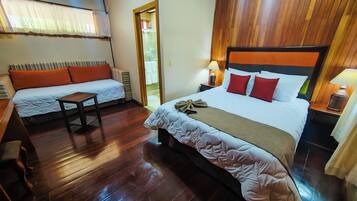 A hotel room with a large bed, a smaller sofa, wooden flooring, and a wooden ceiling.