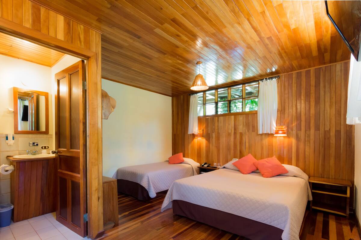 A wooden-floored room with two beds, a wooden wardrobe, a mirror, and a window with curtains.