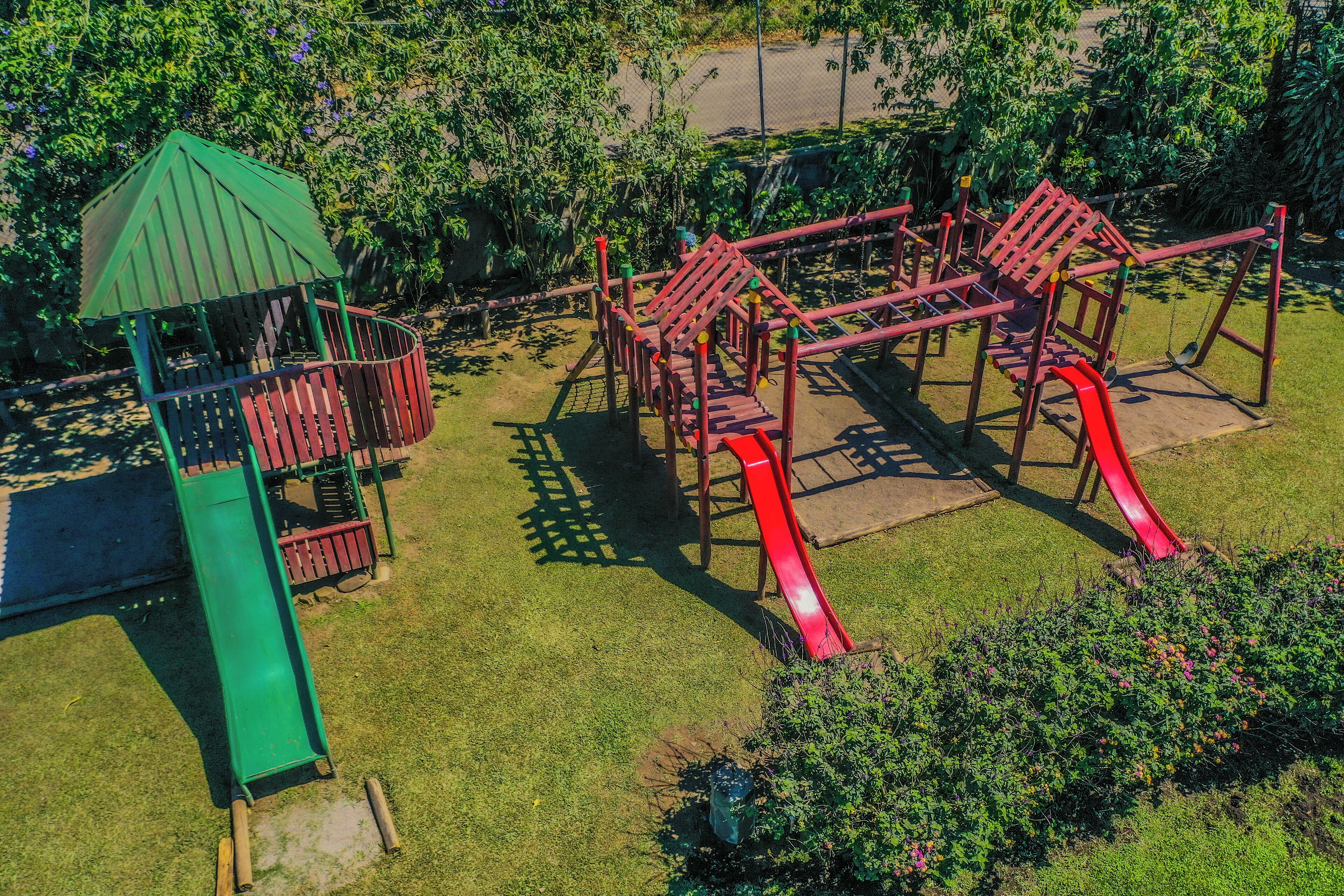 A playground with a green climbing structure, red slides, and a jungle gym.