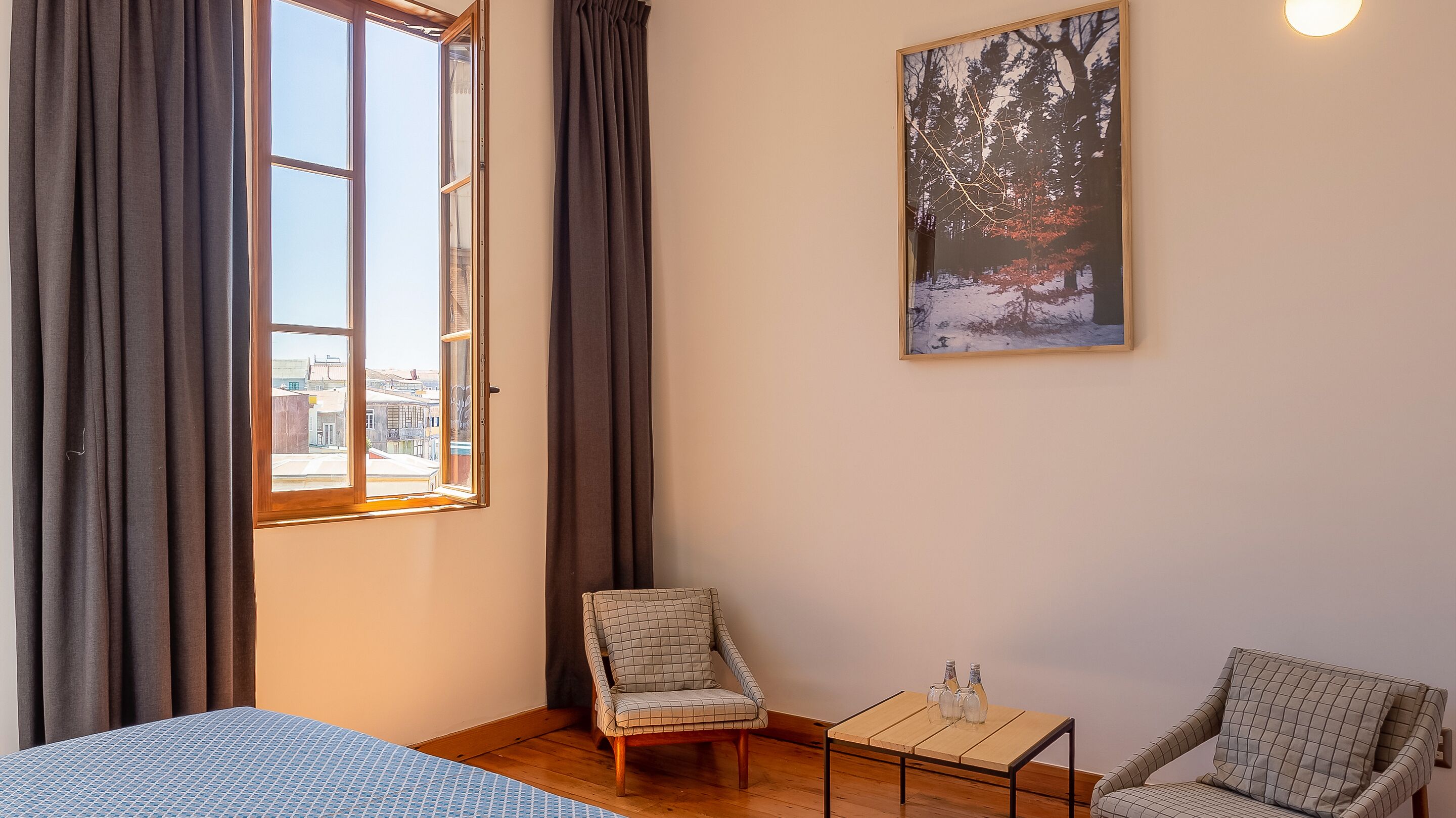 Una habitación con una cama, dos sillas, una mesita y un cuadro en la pared.