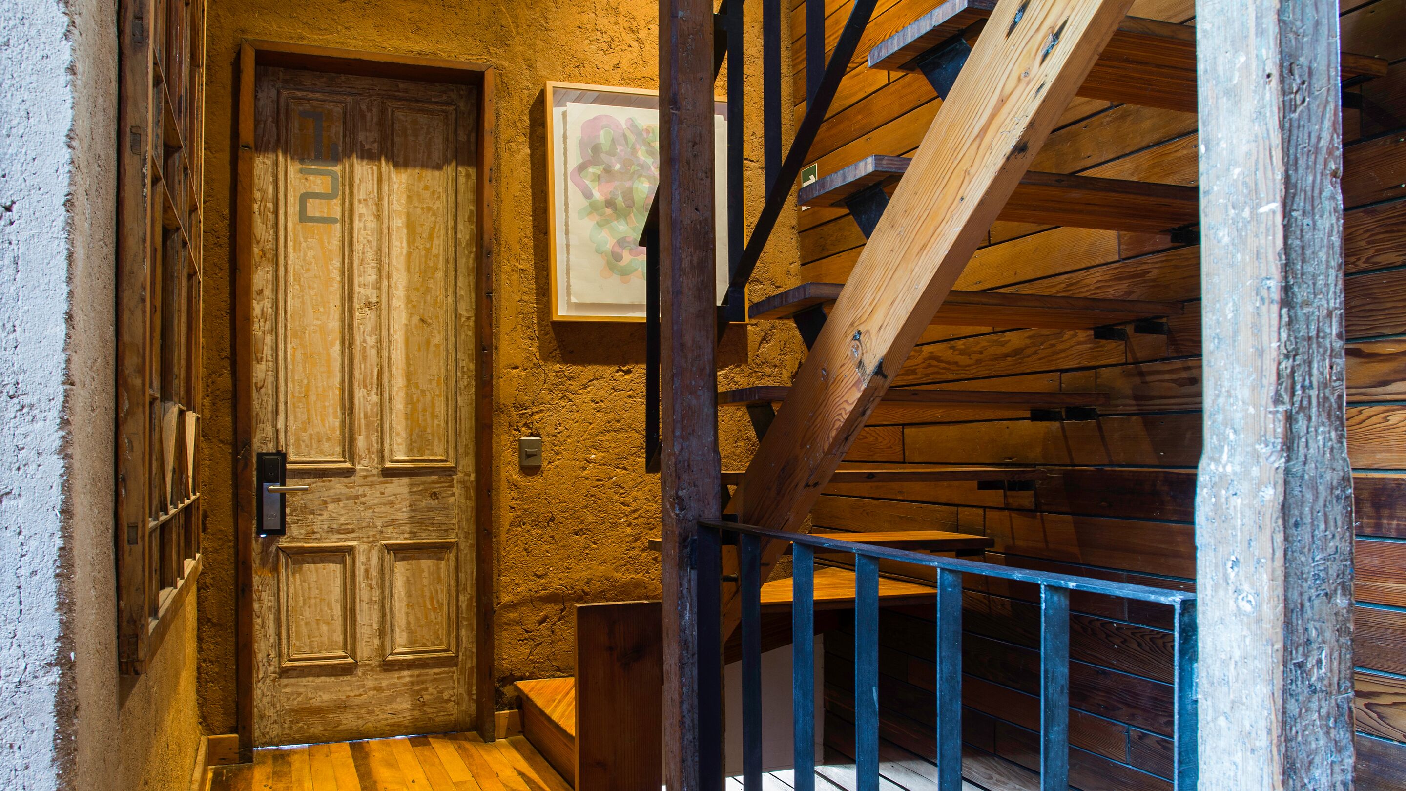 Una escalera de madera con barandilla metálica que lleva a una puerta con el número 2.