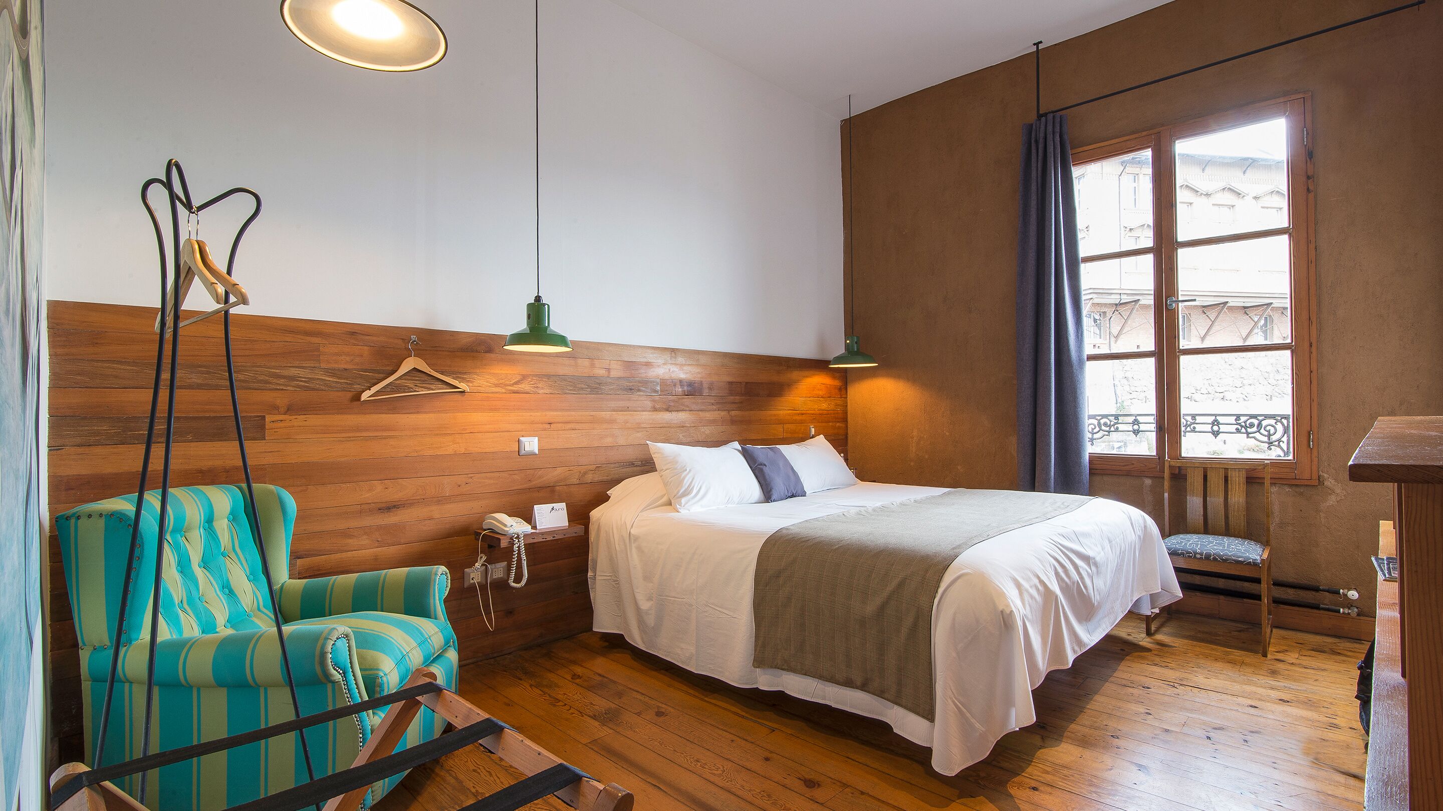 Ein Zimmer mit einem Bett, einem Hängesessel, einer Holzwand, einem Fenster mit Ausblick und einer Pendelleuchte.