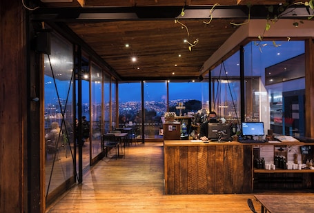A modern interior with a wooden ceiling, large windows, a bar area, and a view of a cityscape at dusk.