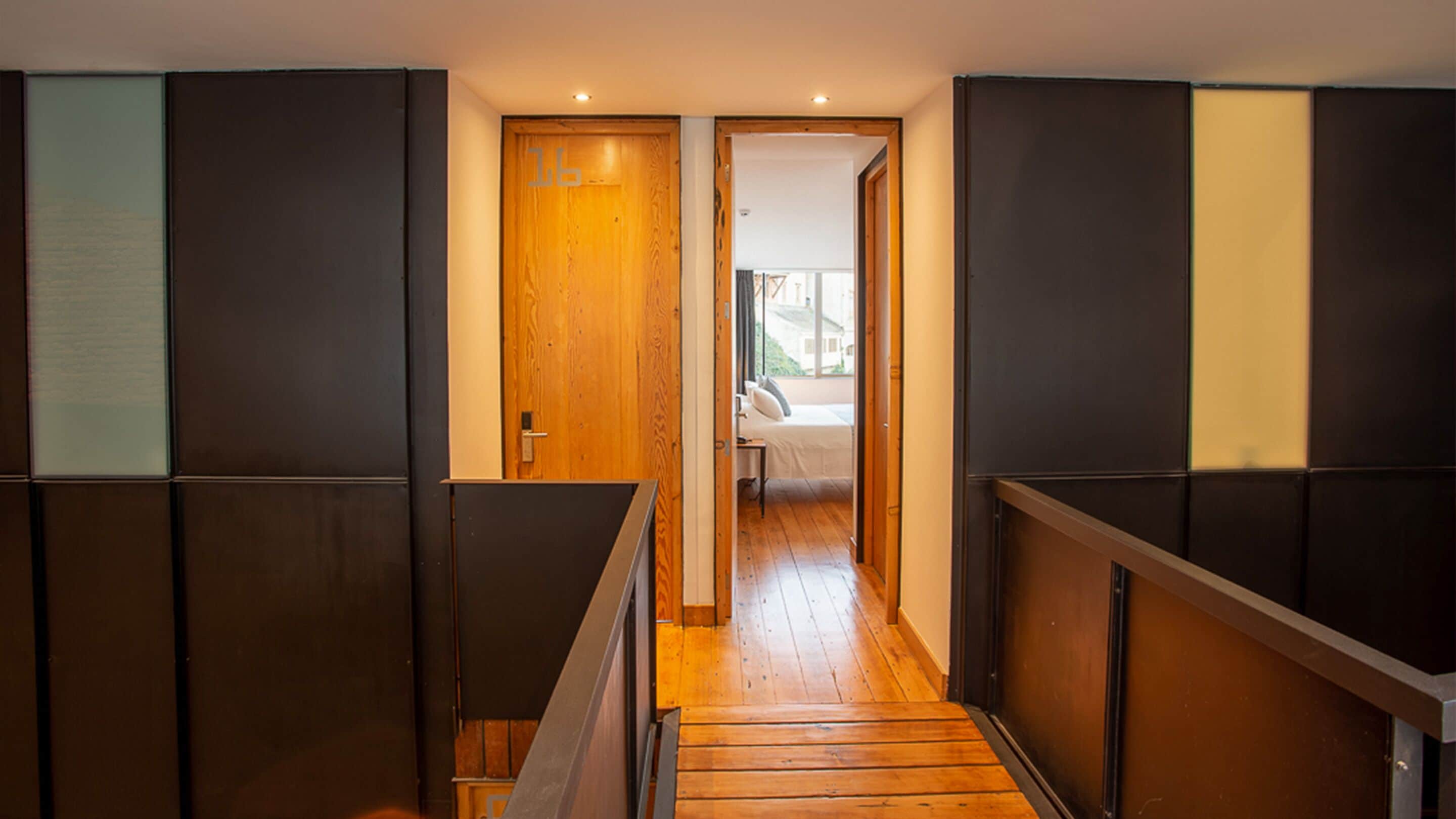Un pasillo con piso de madera y vista a un dormitorio con cama y ventana.