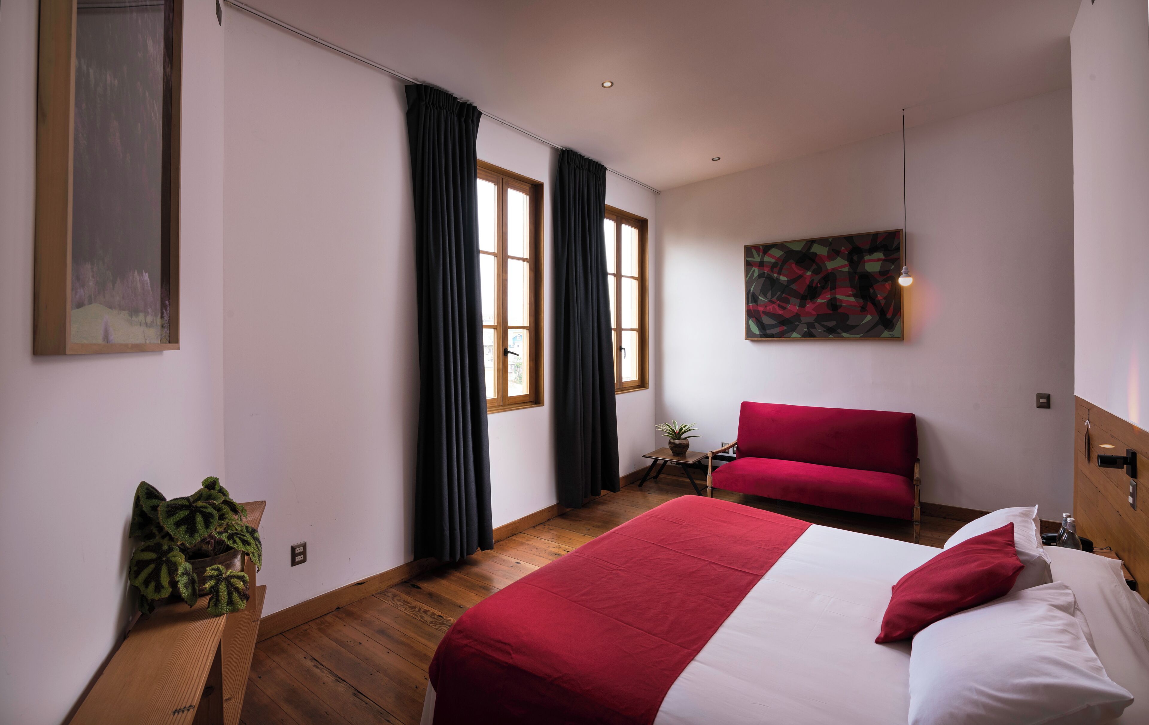 Habitación de hotel con una cama grande, una silla roja, una mesita con una planta y un cuadro en la pared.