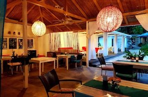 Un'area pranzo interna con tavoli e sedie, una ventola a soffitto e illuminazione decorativa.
