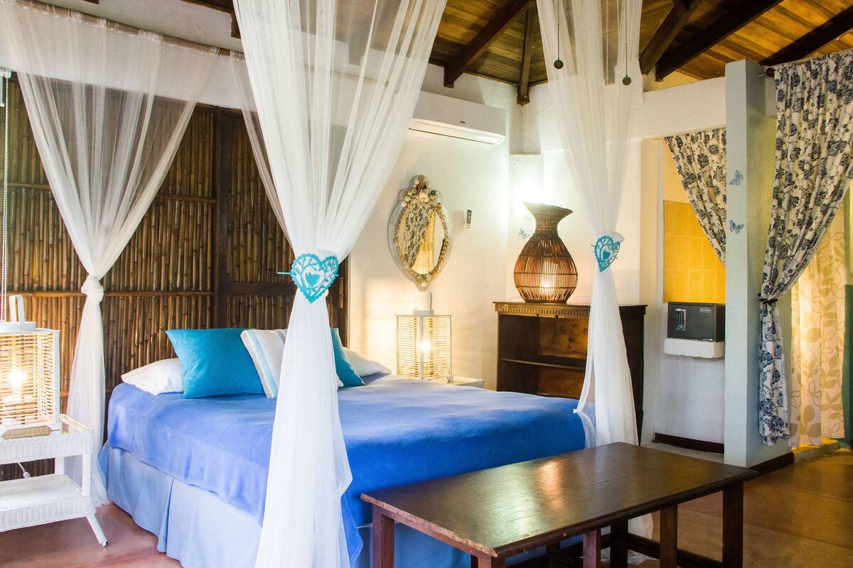 A bedroom with a bed, a bedside table, a lamp, and curtains.