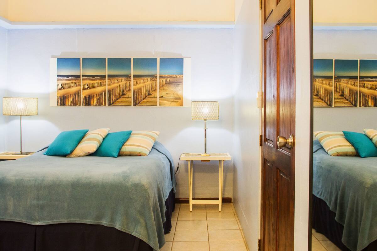 A hotel room with a bed, two bedside tables, a lamp, and a large framed picture on the wall.
