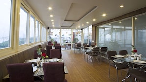 A restaurant with a long dining area, large windows, and hanging plants. - Trimrooms Palm D'or (New Delhi)