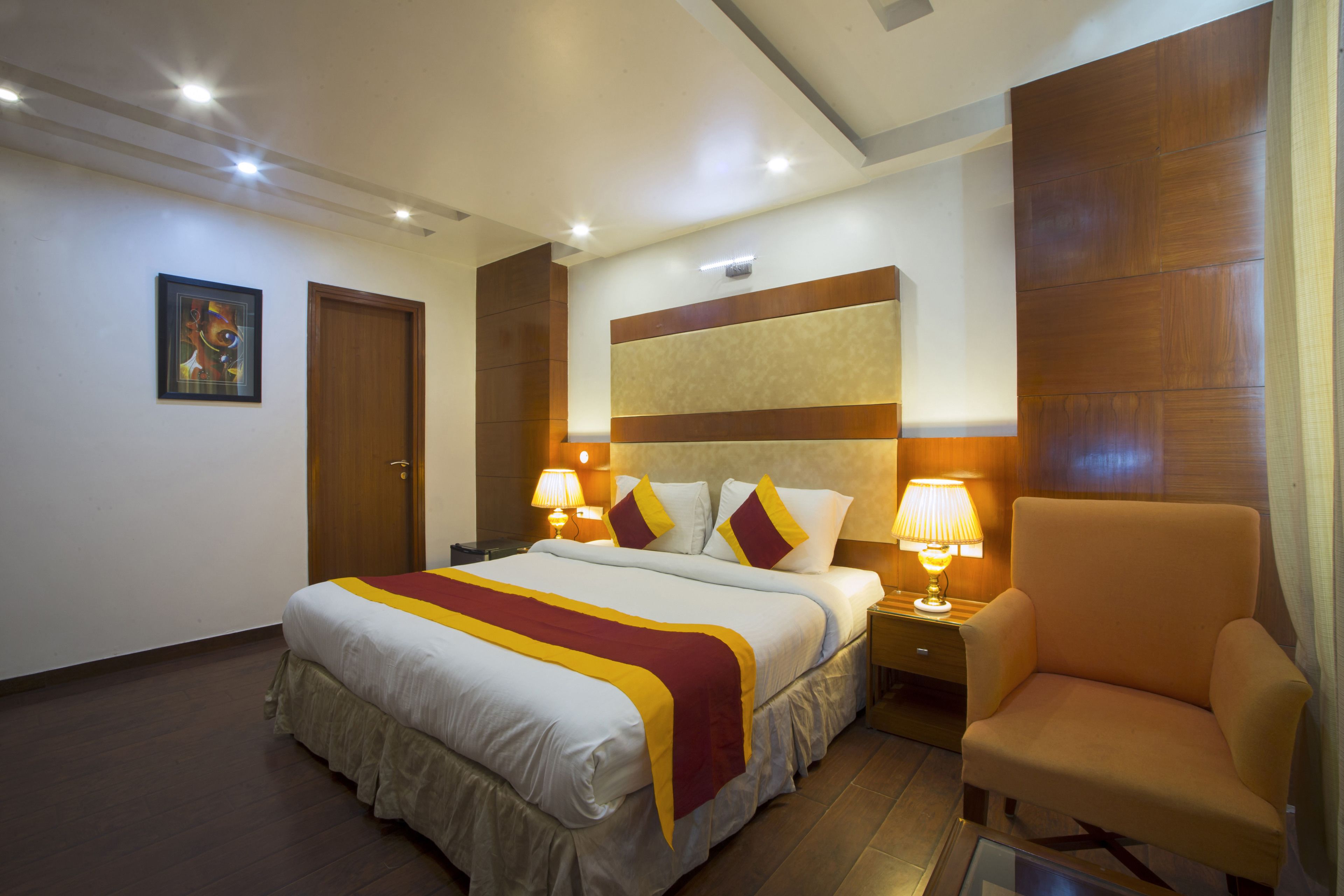 A hotel room with a large bed, two bedside lamps, a wooden headboard, and a chair.