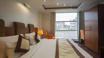 A modern hotel room with a large bed, a sitting area with a chair, and a view of the city through large windows.