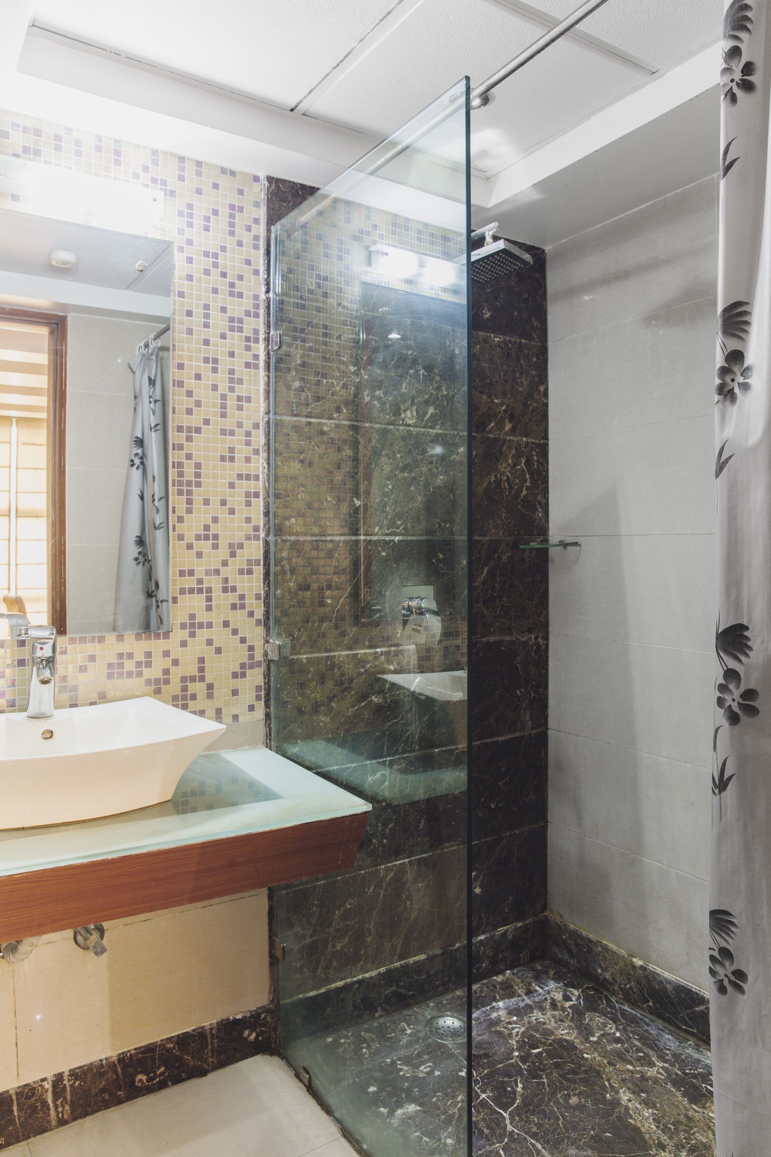 A bathroom with a glass-enclosed shower, a sink with a marble countertop, and a tiled wall with a floral pattern.