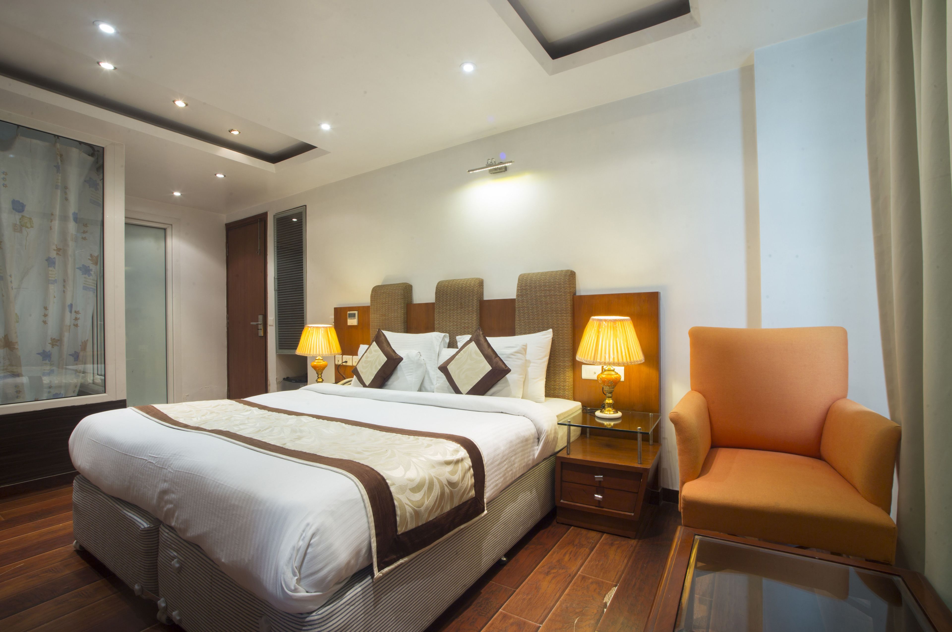 Una camera d'albergo con un letto grande, due comodini con lampade, una sedia e un'ampia finestra con tende.