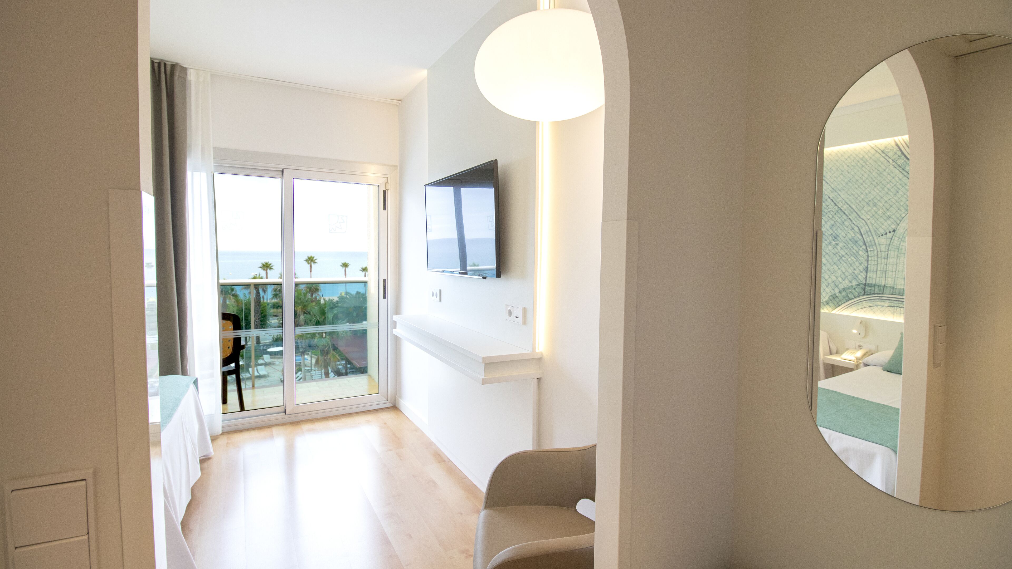 A hotel room with a balcony, a TV mounted on the wall, and a large mirror.