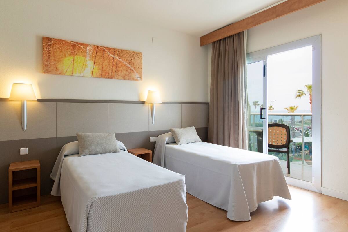 Une chambre d’hôtel avec deux lits, un tableau au mur et un balcon avec vue.