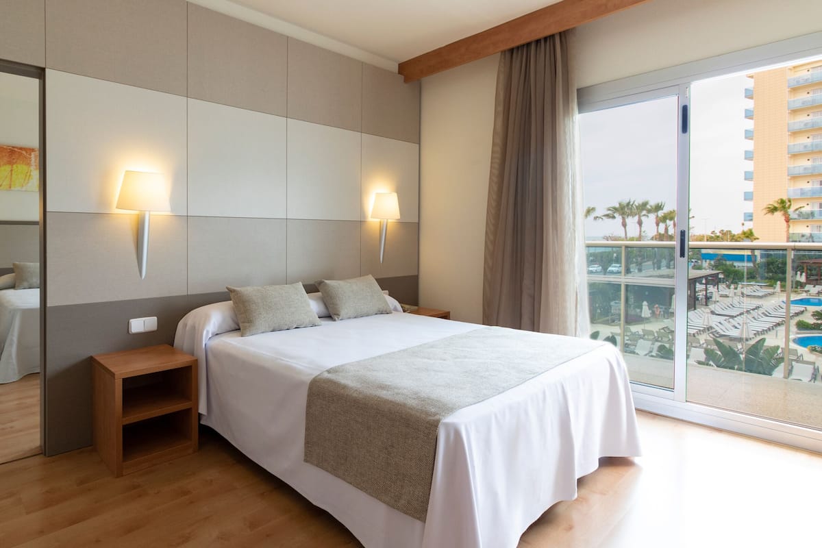 Une chambre d’hôtel avec un grand lit, une table de chevet, un miroir et une vue sur une piscine et des immeubles.