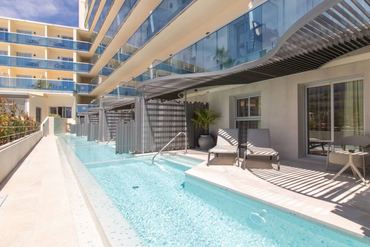 Un espace piscine offrant une vue dégagée sur la piscine, des chaises longues et un bâtiment moderne doté de balcons.