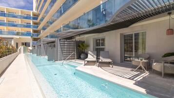 Zona de piscina con vista despejada, sillones de descanso y un edificio moderno con balcones.