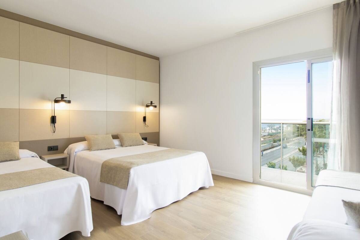 Une chambre d’hôtel avec deux lits, une grande fenêtre donnant sur un beau paysage et des lampes fixées au mur.
