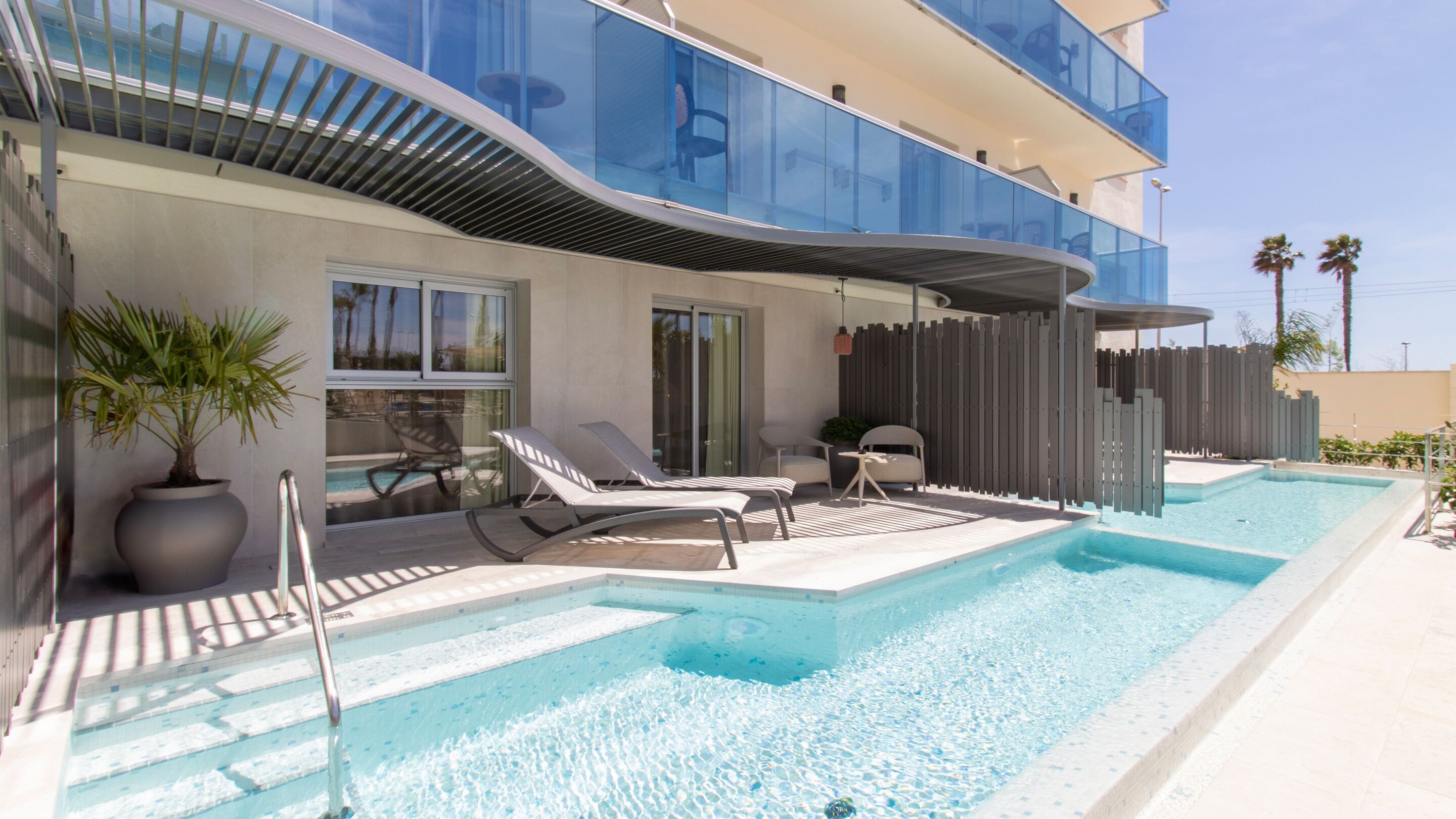 A modern hotel with a swimming pool, lounge chairs, and a potted plant.