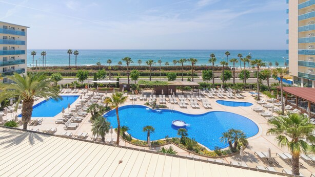 A resort with a large swimming pool, sun loungers, and a view of the ocean. - Golden Taurus Aquapark Resort (Pineda de Mar)