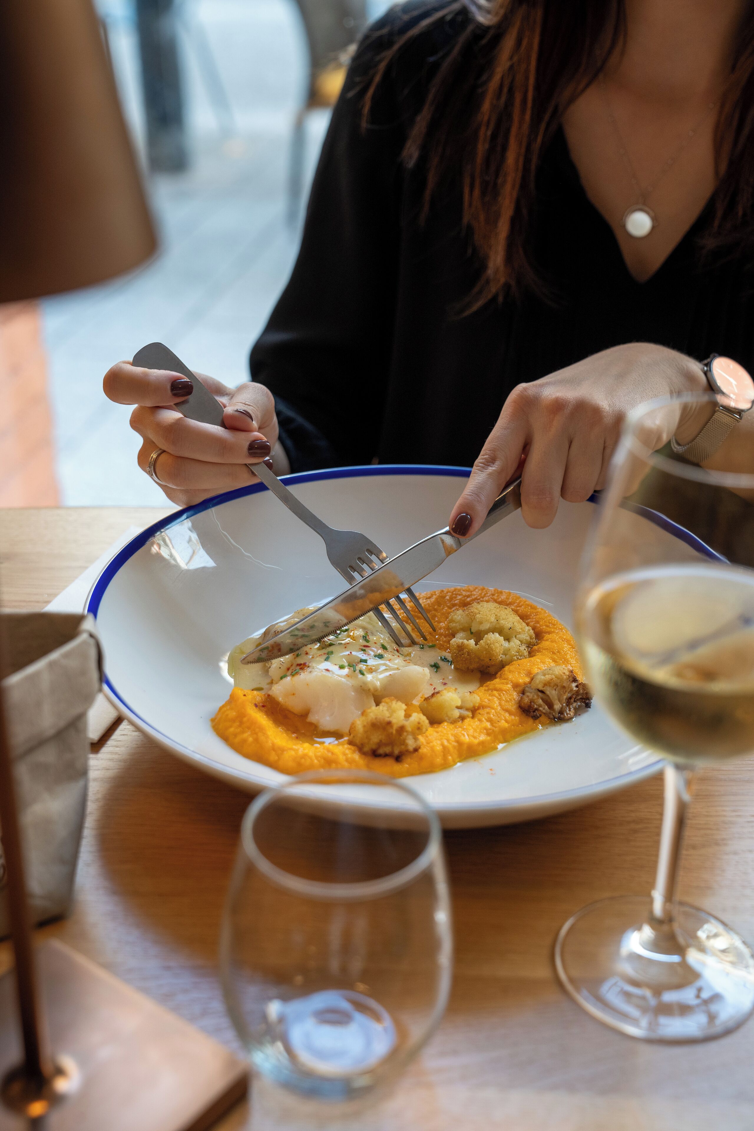 Una persona comiendo en una mesa, con un plato de comida, un tenedor y una copa de vino.