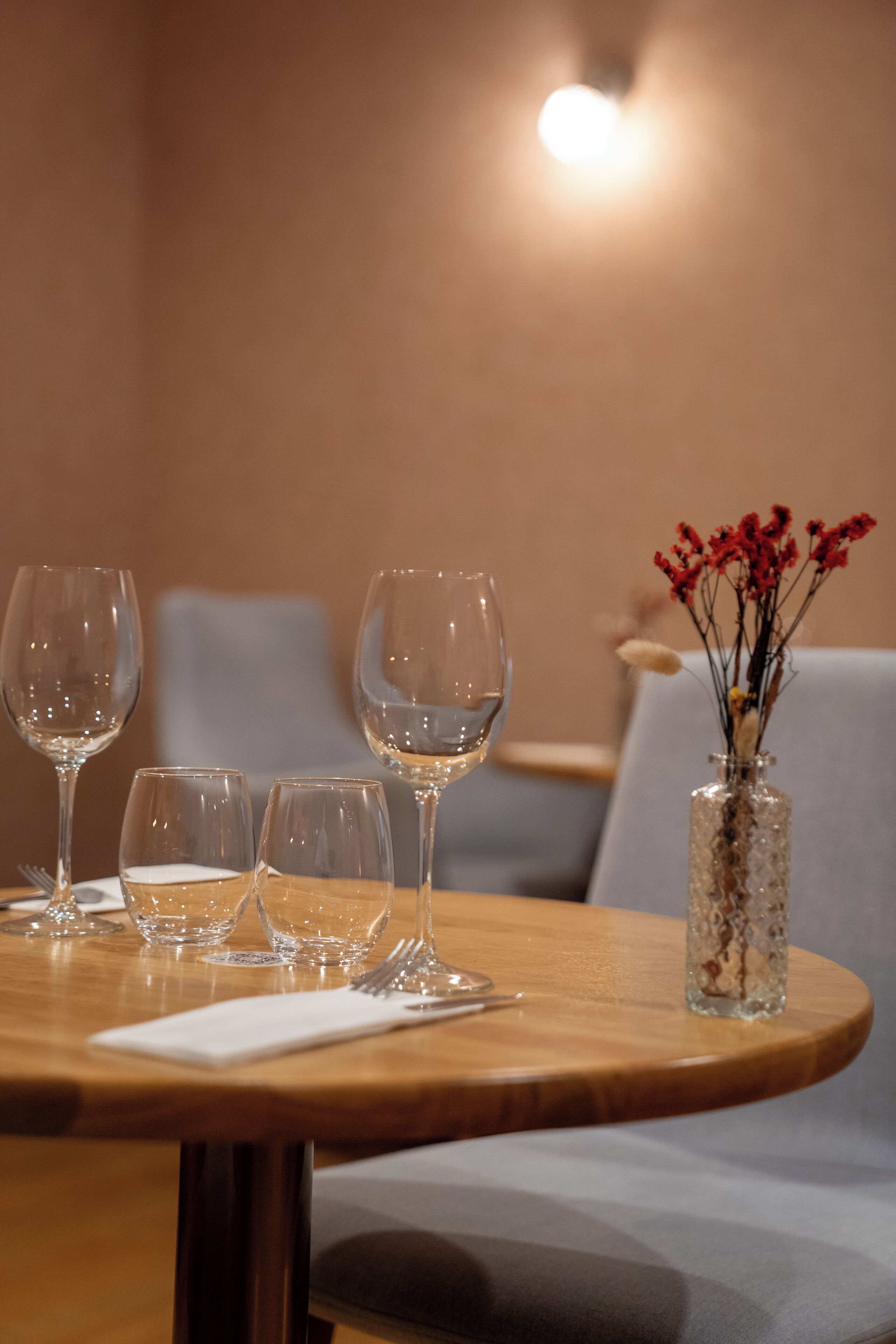 A dining table with four wine glasses and a vase with red flowers.