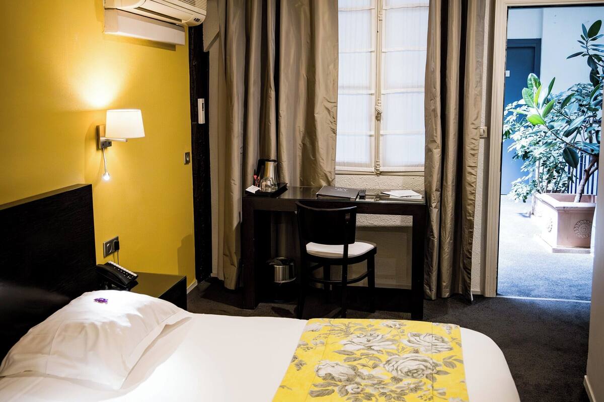 Een hotelkamer met een bed, bureau, stoel en raam met gordijnen.
