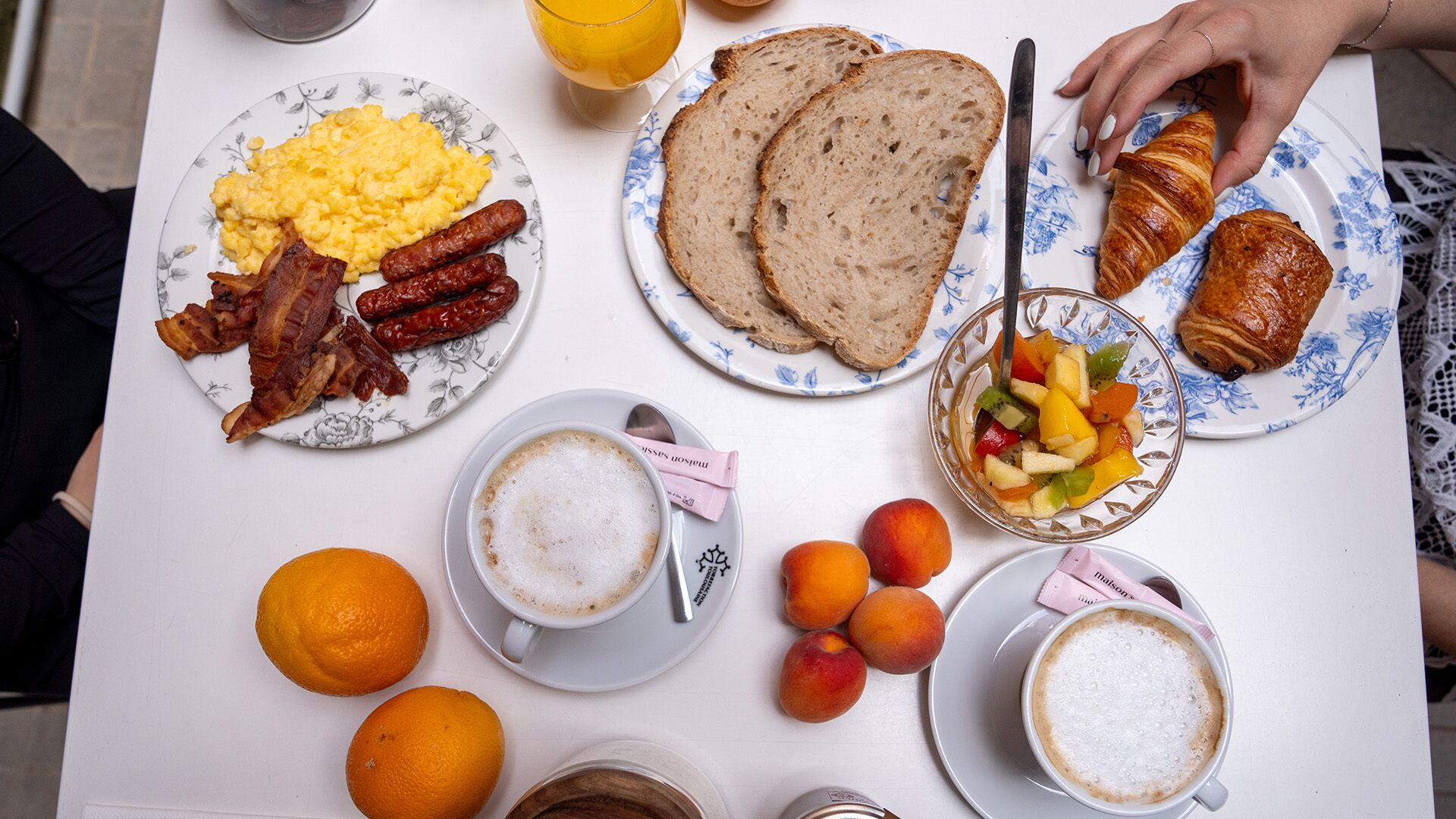 Ein Frühstückstisch mit Rühreiern, Würstchen, Toast, Croissants, Obst und Kaffee.