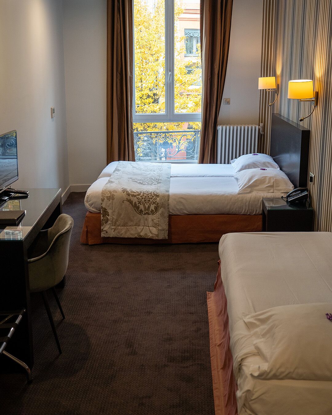 Une chambre d’hôtel avec deux lits, un bureau, une chaise, une télévision et une fenêtre avec des rideaux.
