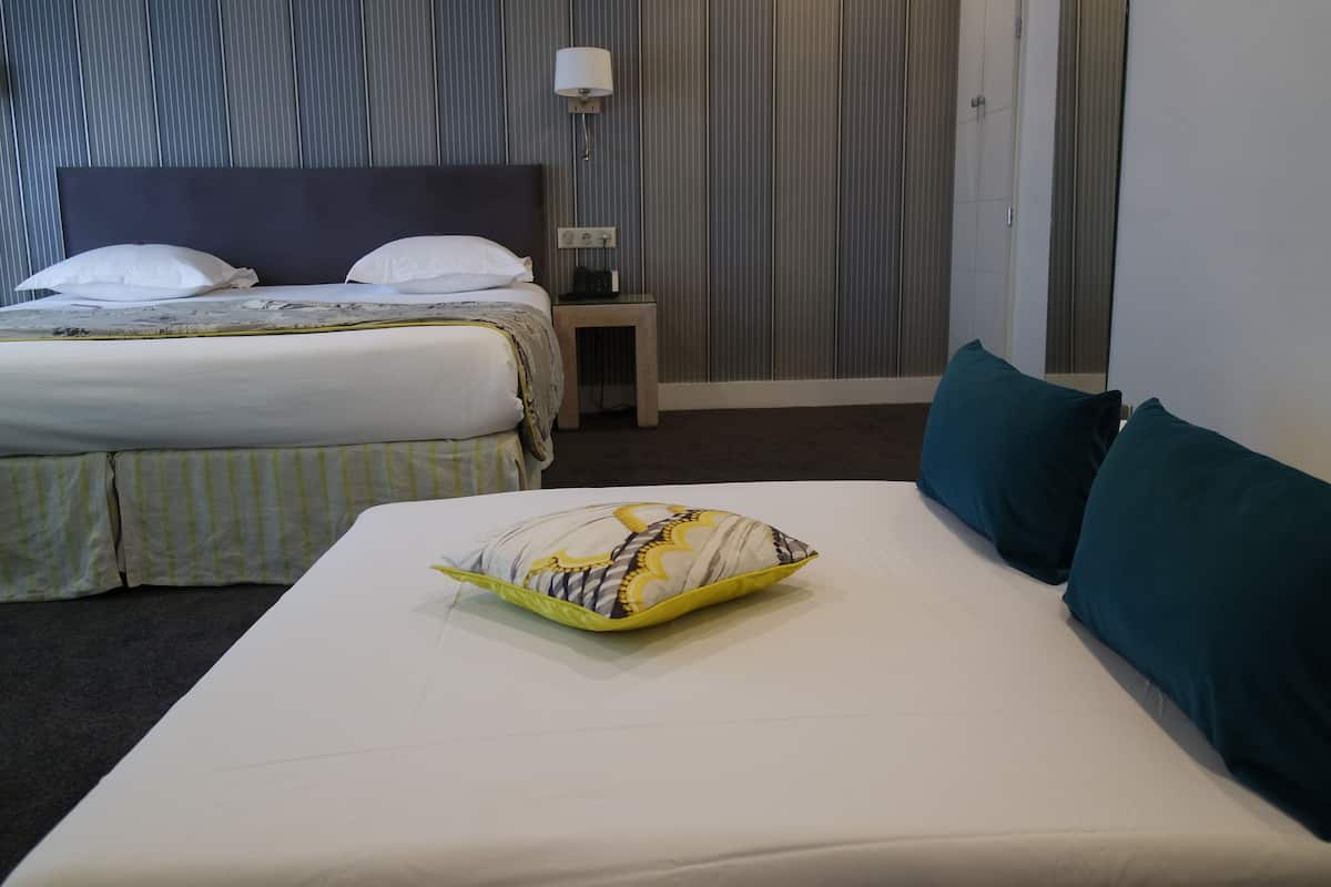 Een hotelkamer met twee bedden, een nachtkastje met een lamp, en een gestreept kussen op het grotere bed.