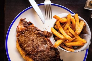 A plate with a steak and fries, a fork, and a knife.