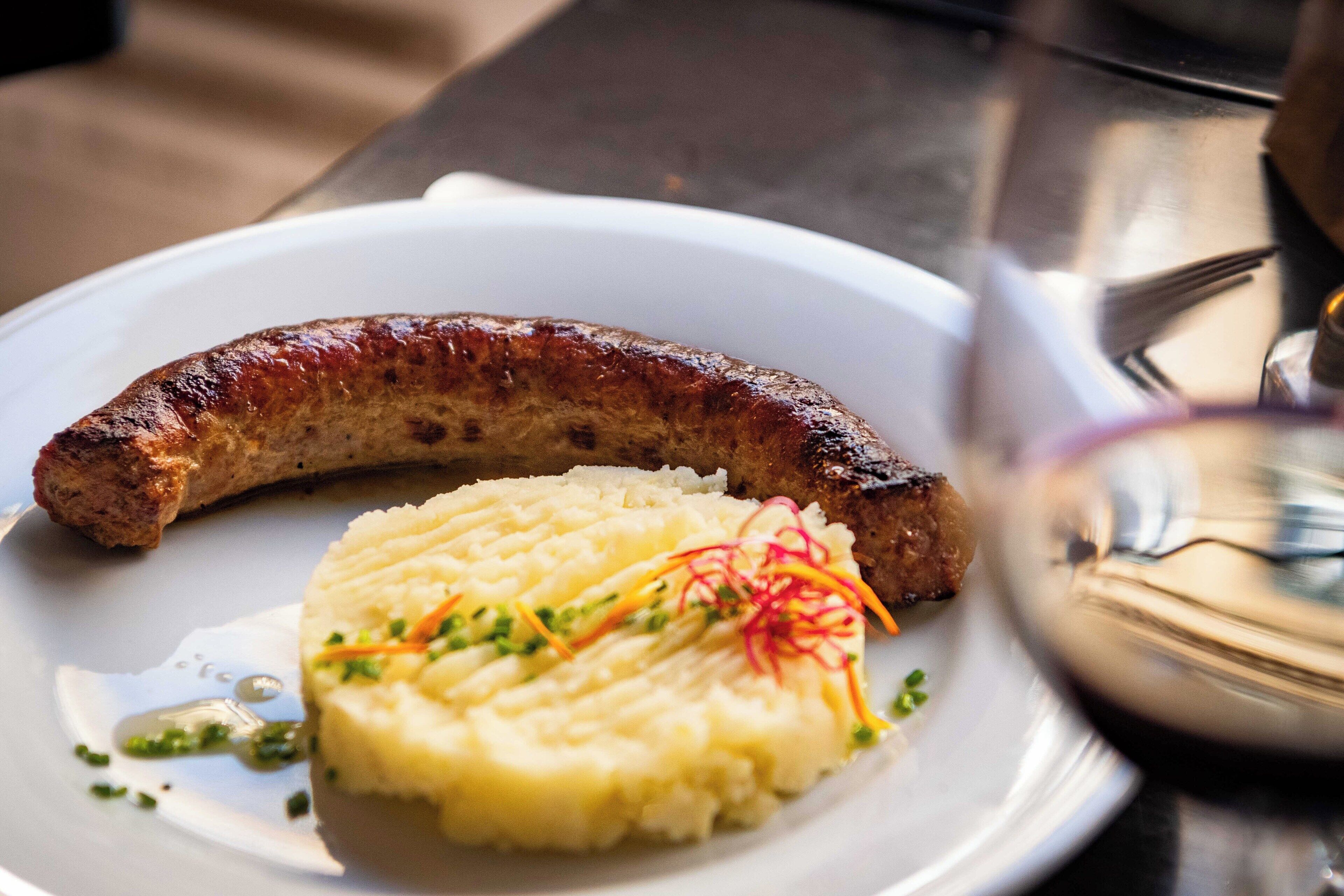 Un plato con salchicha a la parrilla y puré de papas adornado con hierbas.