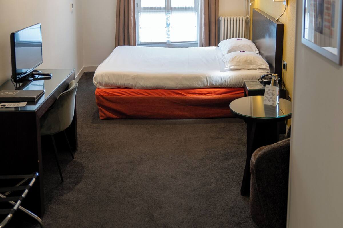 Een hotelkamer met een bed, een bureau, een stoel, een televisie en een raam met gordijnen.